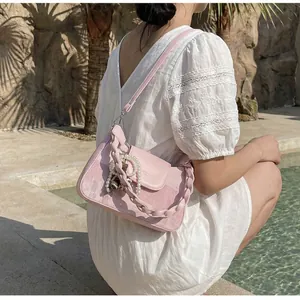 Detail of pink leather bag with braided handle and pearl charm in outdoor setting