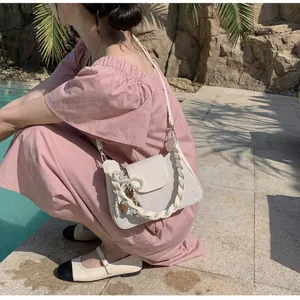 Detail of a beige square bag with pearl charm and bear pendant by the pool