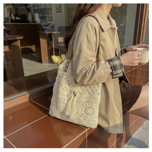 Detail of hollow-out woven tote bag with fringe charm and slim brown leather strap