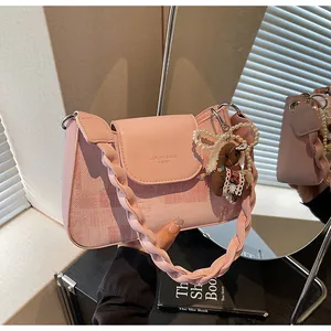 Detailed view of pink leather bag featuring woven strap, pearl chain, and plush charm