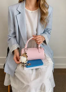 Detail of light pink cylinder handbag featuring silver rings and cream plush charm