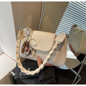 Detail of cream crossbody bag featuring woven strap and pearl horse charm attachment
