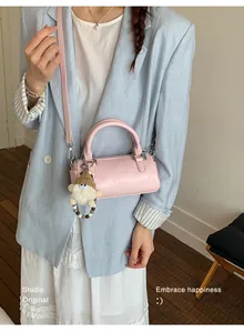 Pink cylinder boston bag with plush doll charm shown with a casual fashion outfit