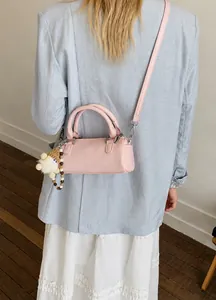 Pink cylindrical barrel bag with a knitted doll charm shown on a female model