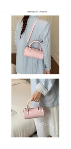 Detail view of pink cylindrical crossbody bag with top handle and smooth metal zipper