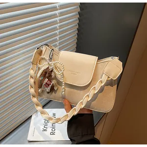 Detail of cream shoulder bag with braided strap, pearl chain and horse charm accessory