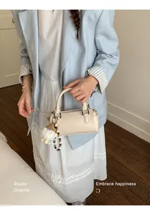 Detail of minimalist cream cylindrical handbag with cute doll charm and pearl strap detail