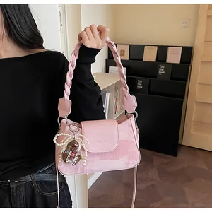 Close-up of pink shoulder bag featuring a woven handle and a pearl bear charm detail