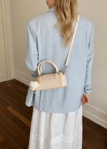 Cream white cylinder bag with top handles and plush charm worn by model in a studio