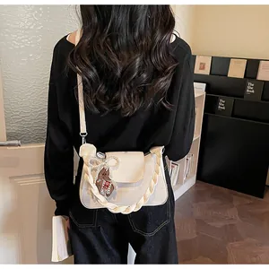 Detail showing cream crossbody bag with woven handle, leather charms, and flap closure