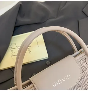 Close-up of beige water ripple bucket bag featuring pleated side details and silver logo