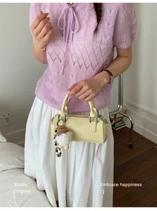 Pale yellow leather cylinder handbag styled with pearl plush charm on casual outfit