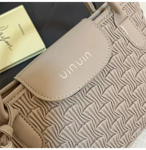 Close-up of beige water ripple bucket bag with pleated texture and gold logo detail