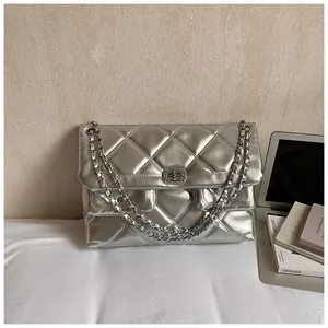 Detail of silver quilted leather bag with chain strap next to laptop and magazine