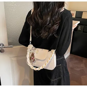 Detail of cream crossbody bag with woven strap and pearl bow charm on model back