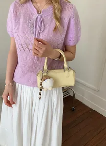Detail of light yellow leather cylinder bag with soft white fur ball charm accessory