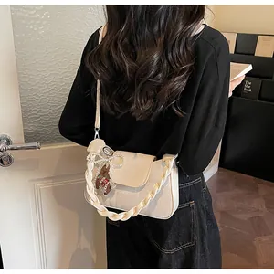 Detail of cream crossbody bag featuring woven texture and pearl bow bear charm