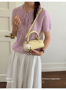 Detail of yellow cylindrical crossbody bag with plush charm on a fashion model