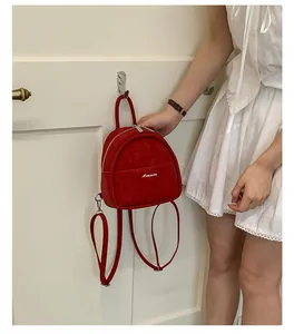 Detail of red mini backpack with suede texture and metal zipper hanging on a door