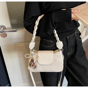 Detail of cream square bag with braided handle, pearl bow and bear charm decor