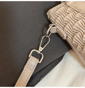 Detail of light beige bucket bag showing gold metal lobster clasp and pleated leather texture
