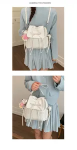 Detail view of white PU leather backpack with ribbon bow and plush bear keychain accessory