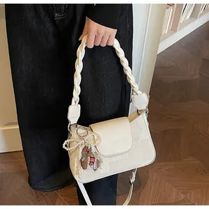 Detail of cream leather handbag featuring woven handle and a pearl bow bag charm