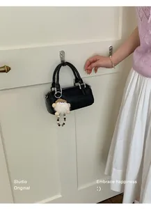 Detail view of a black pebble leather barrel bag hanging on a hook with a cute plush pendant
