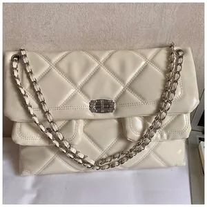 Detail view of cream quilted bag with silver chain strap and metal lock closure