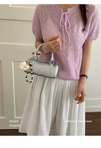 Close-up of silver cylinder handbag featuring a plush pompom and beaded chain detail