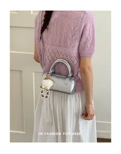 Close-up of a silver metallic cylinder handbag with a plush charm and fine strap details
