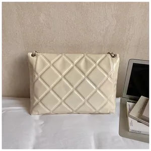 Detail of cream quilted crossbody bag with silver eyelets next to a laptop on a desk
