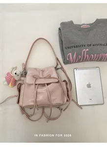 Detail of pink drawstring backpack with bow accent and plush bunny charm on fabric background