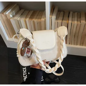 Detail of cream crossbody bag with pearl strap, pony charm and woven shoulder strap