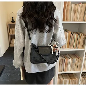 Detail of black crossbody bag with textured panel, twist handle and pearl charm accessory