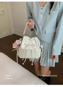 Detail of a beige bow drawstring backpack with a cute bear charm on a female model