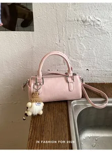 Pink cylindrical Boston bag with a furry gnome charm on a wooden surface in soft light