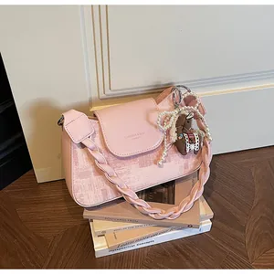 Pink shoulder bag detail with woven strap, pearl bow charm and pony doll pendant