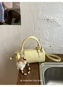 Detail of a light yellow cylinder bag with high-quality texture and a plush charm