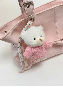 Close-up of white plush bear pendant with pink sweater on a leather handbag detail