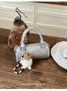Detail of silver metallic barrel bag with plush gnome charm on vintage wood surface