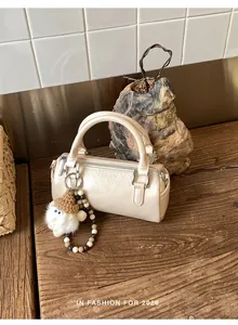 Detail of cream barrel bag with plush pendant and beads on a rustic wooden table