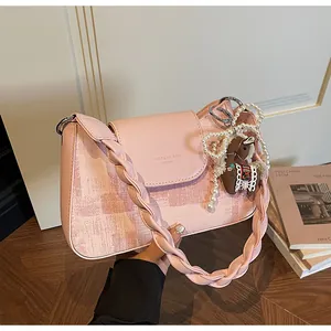 Pink shoulder bag detail with woven leather strap, pearl charms and pony pendant