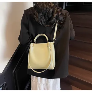 Modella che indossa una borsa a secchiello giallo chiaro su scale in legno con manico oro