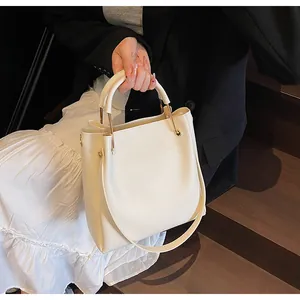 Dettaglio borsa a secchiello bianco crema con hardware dorato su gradini di legno scuro