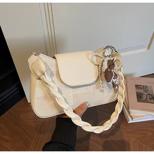 Detail of cream white baguette bag featuring a braided handle and decorative pearl charm