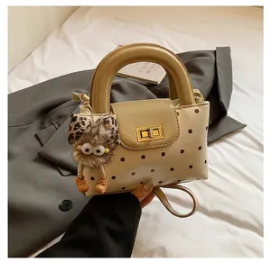 Detailansicht der cremefarbenen Punkte-Handtasche mit Goldschloss und Plüsch-Anhänger