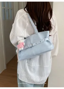 Detail of light blue leather tote bag featuring a decorative buckle and teddy bear charm