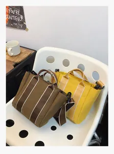 Detail of canvas bucket bag featuring vertical stripes and wide shoulder strap on a chair