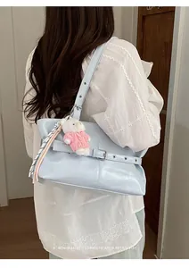 Close-up of light blue glossy tote bag with metal buckle strap and bear charm